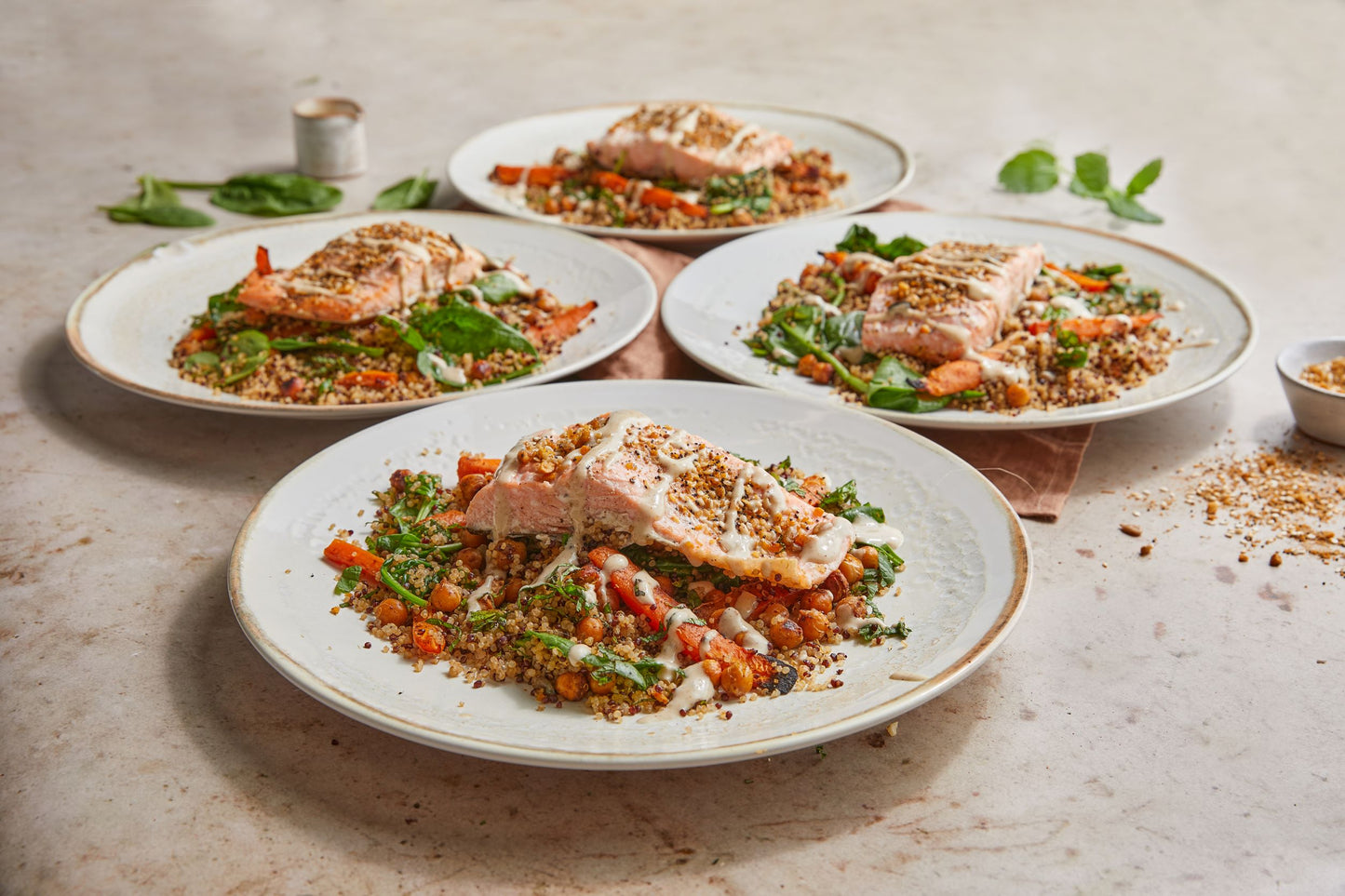 Four plates of salmon on a bed of quinoa with roasted carrots and tahini sauce