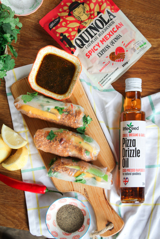 Chopping board with three Mexican summer rolls filled with quinoa, a dish of soy sauce and a packet of Quinola Spicy Mexican on the side with a bottle of Pizza Drizzle oil by Little Seed