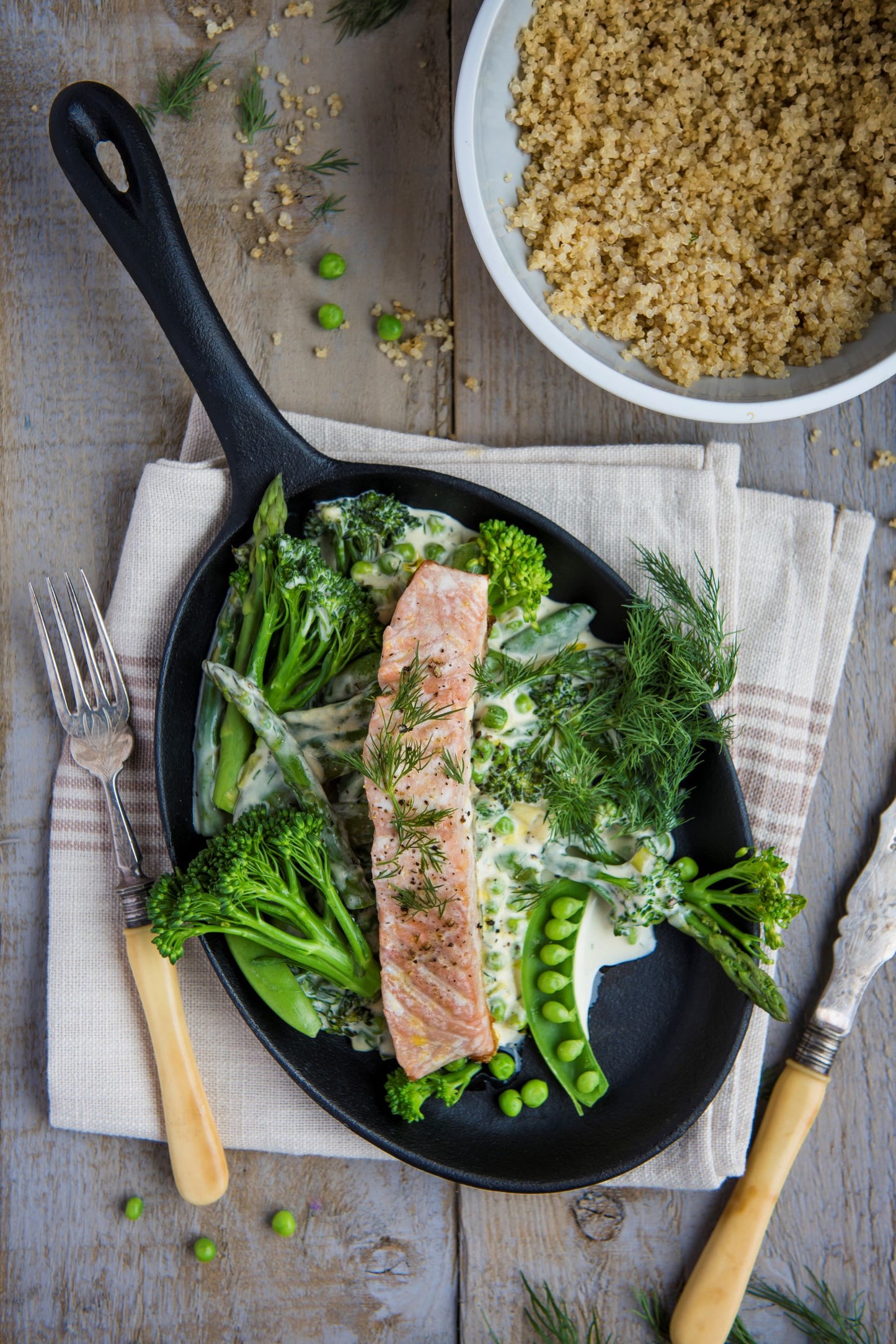 Frying pan with creamy green vegetables and salmon fillet next to a bowl of quinoa