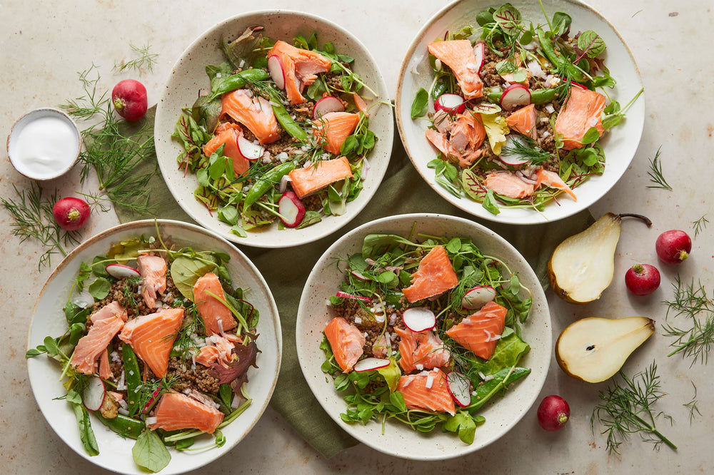 Four bowls of quinoa and lentil salad topped with greens and salmon fillets