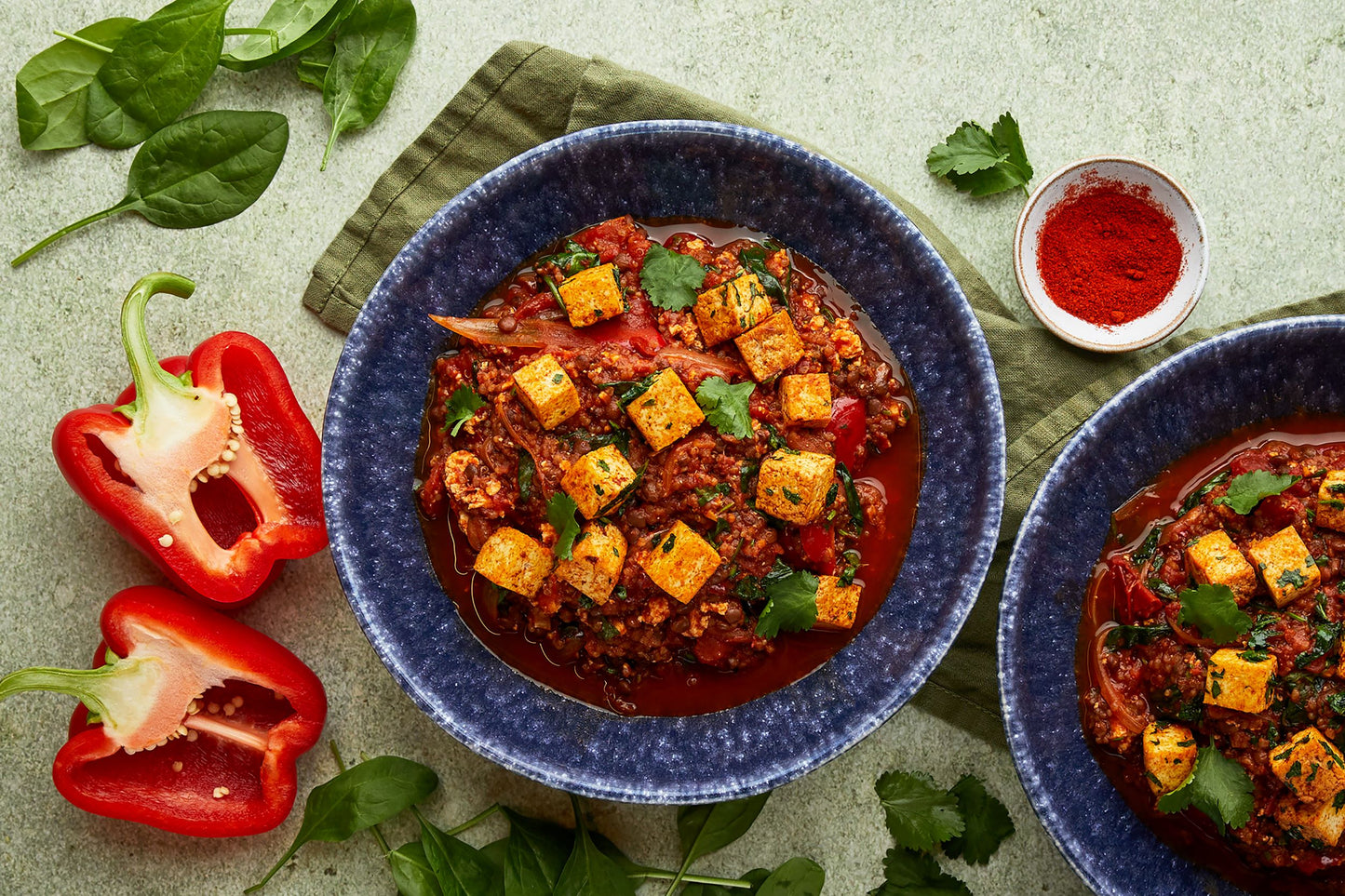 Two bowls of tofu shashuka mixed with quinoa and lentils. Half a cut pepper placed on the side with a green background