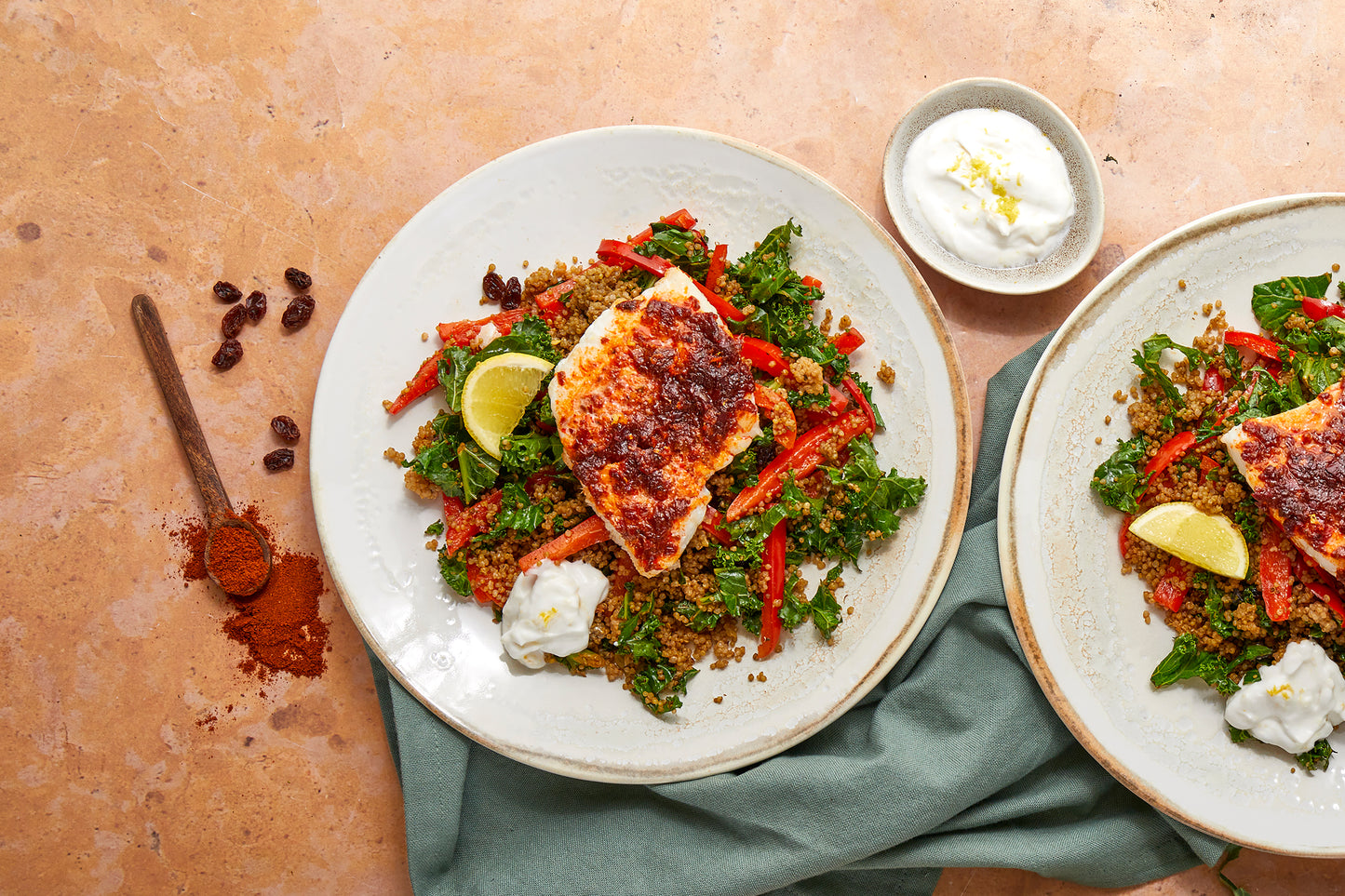 Two plates of marinated cod on a bed of quinoa, with dollops of spiced yogurt