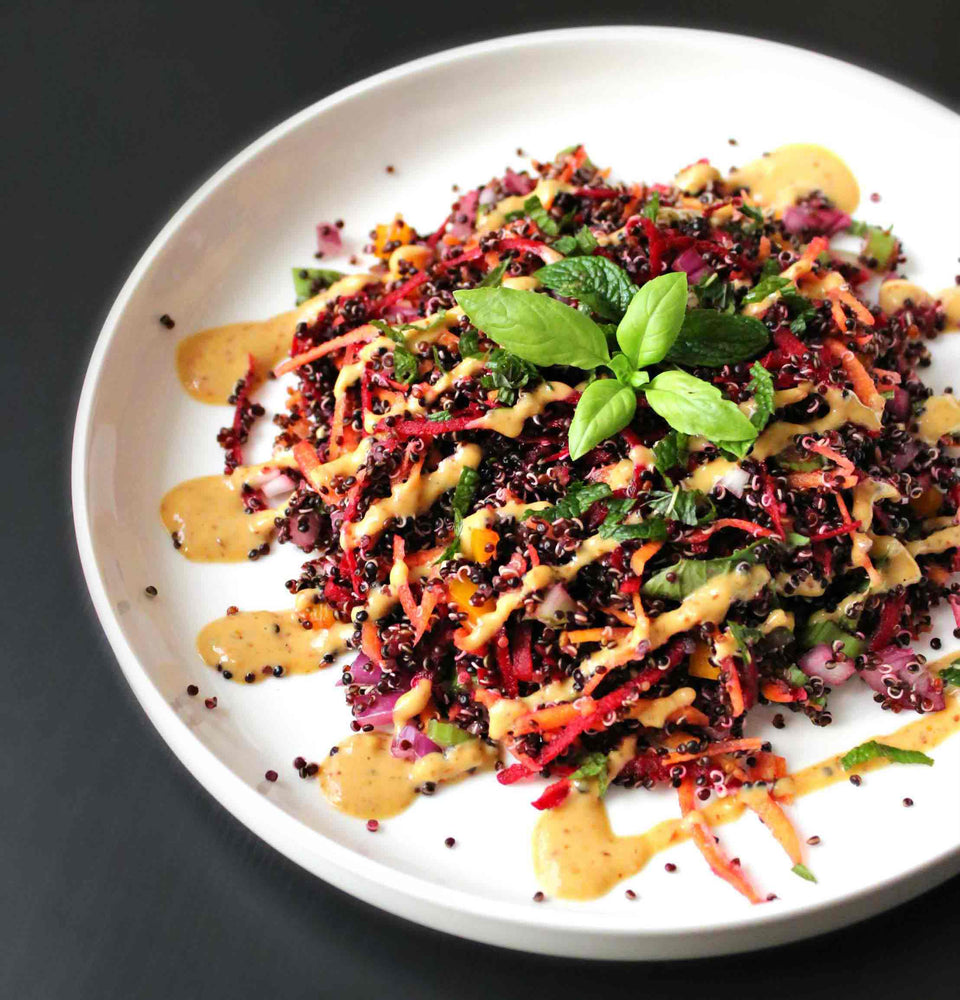 Plate of black quinoa mixed with celelary, onion and grated beetroot. Topped with an orange dressing and four basil leaves  