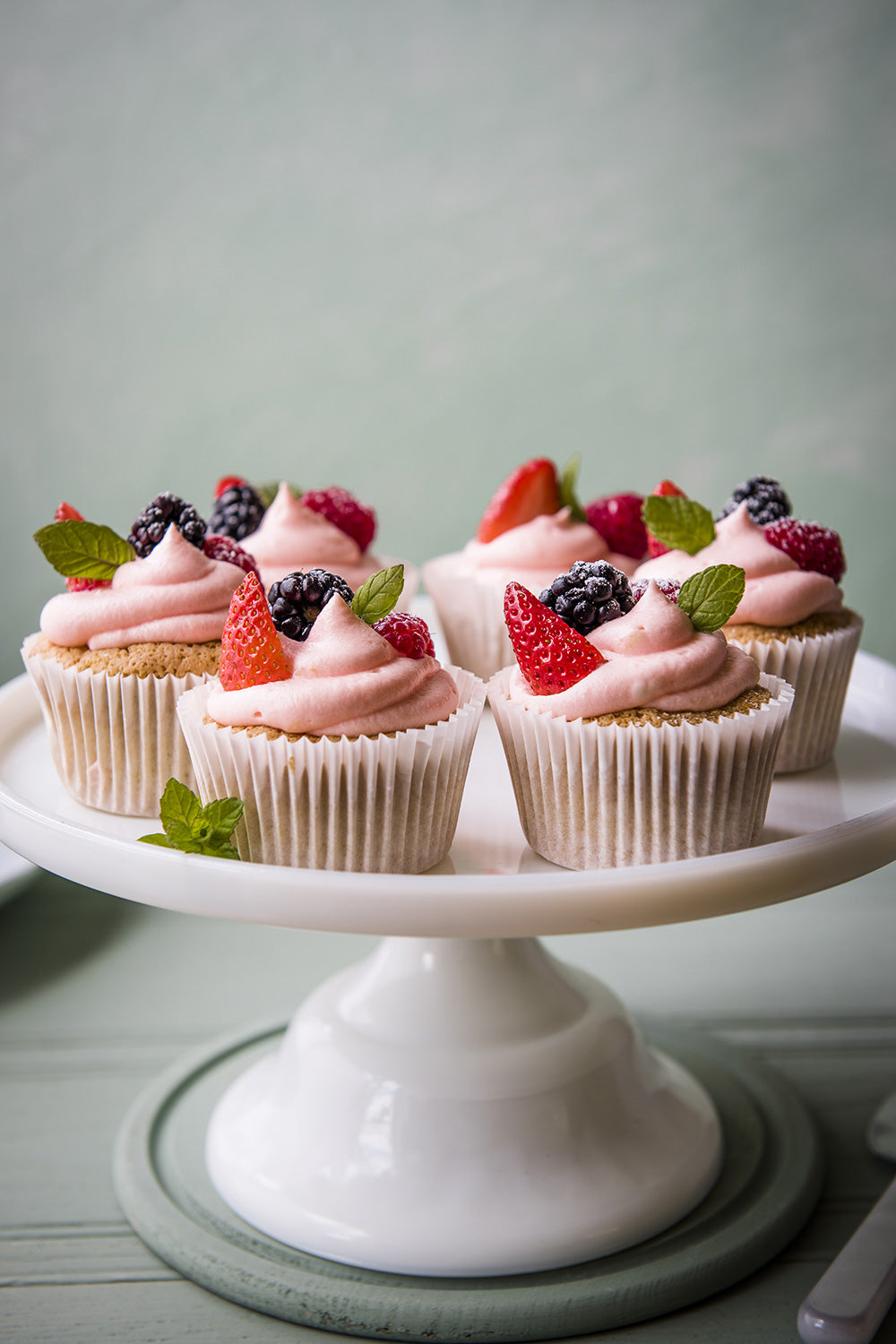 Tray of quinoa cupcakes with pink whipped icing cream with strawberries, raspberries and mint leaves