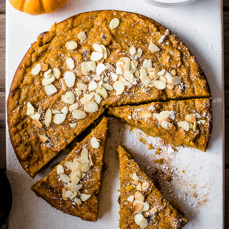 Birds eye view of a quinoa pumpkin cake with flaked almonds and icing sugar dusted on top
