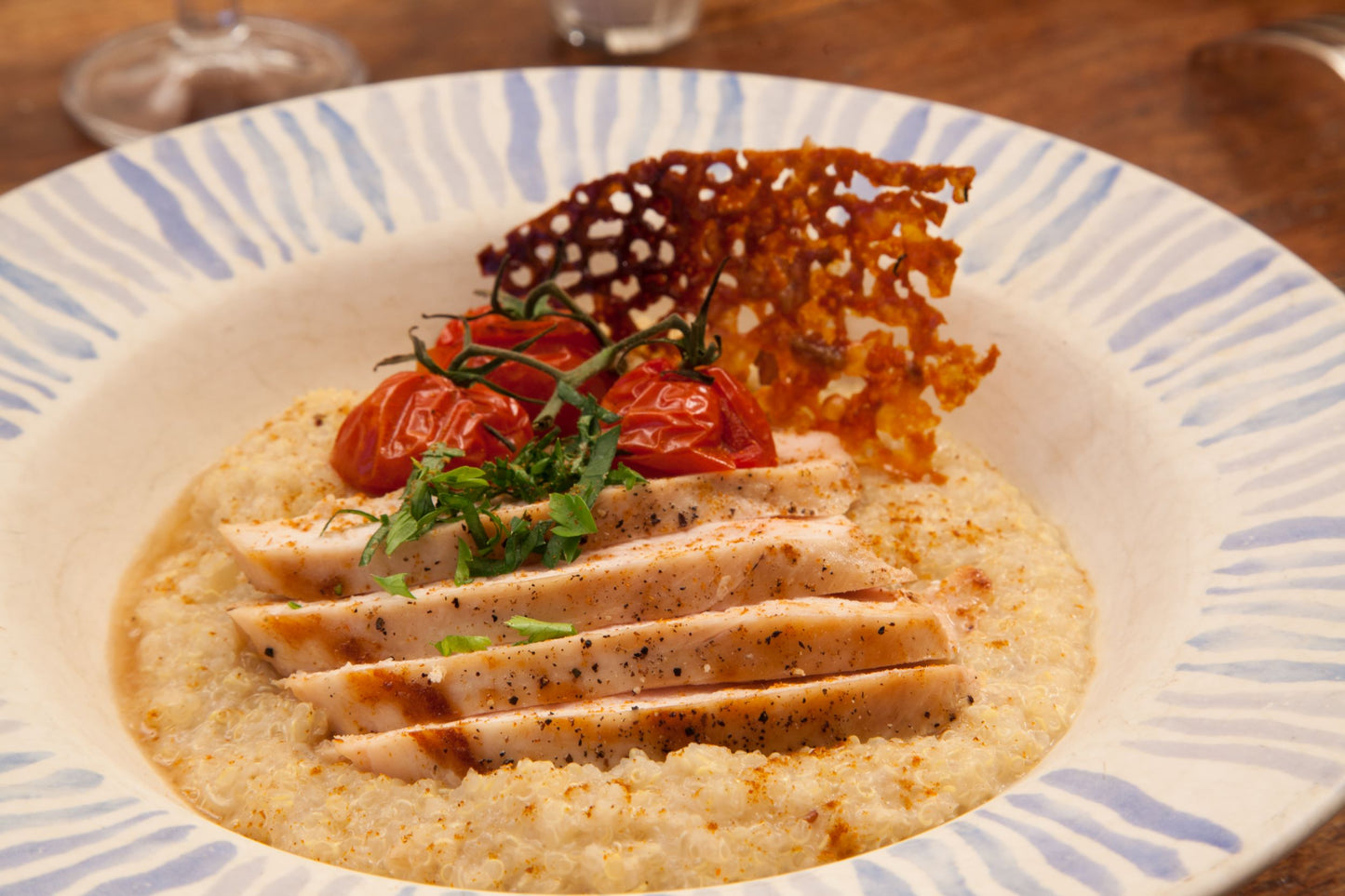 Bowl of creamy chicken and quinoa with tomatoes and Parmesan shard on top 