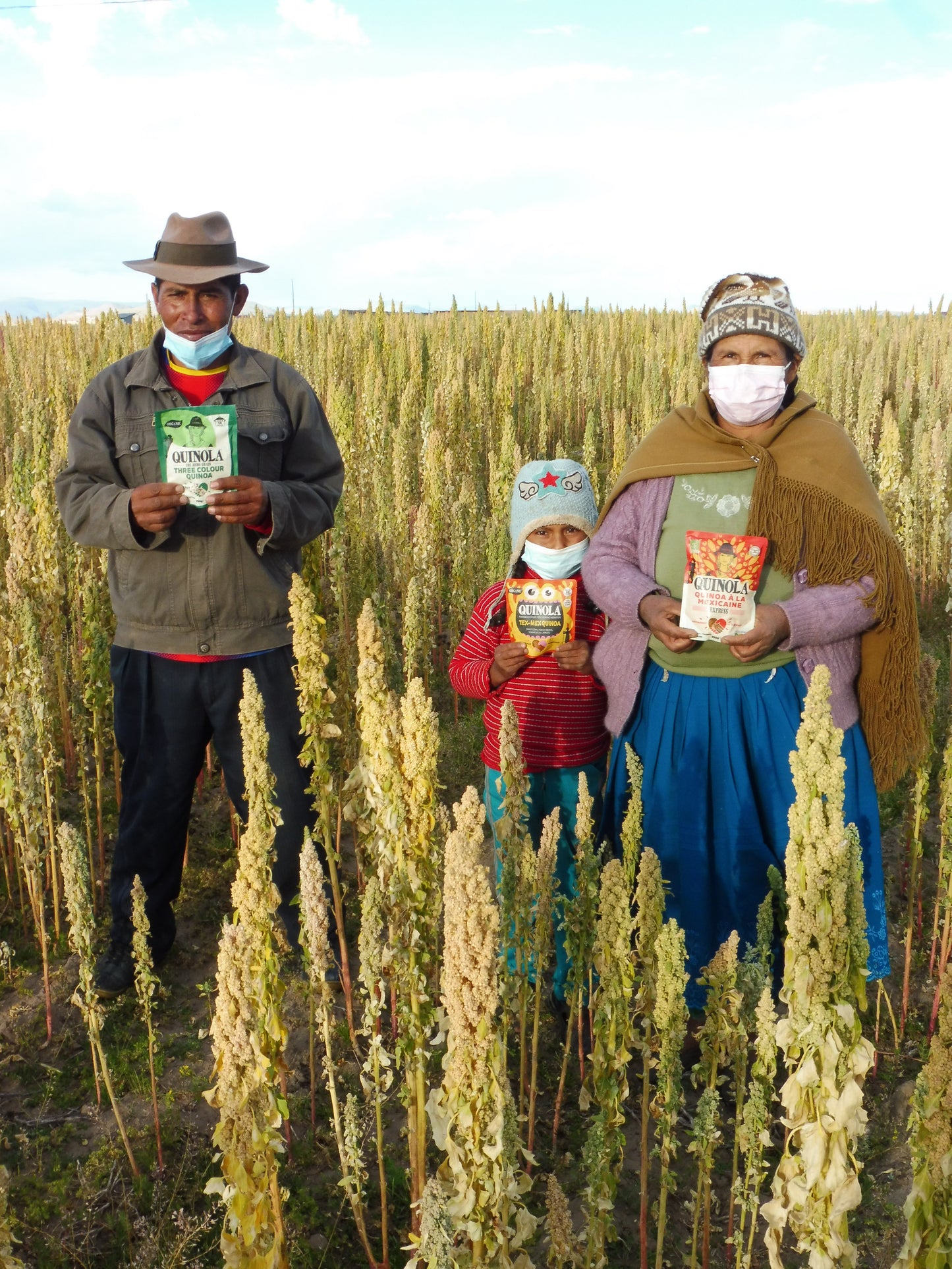 Farmer and farmer family holding quinola packets in front of quinoa field 