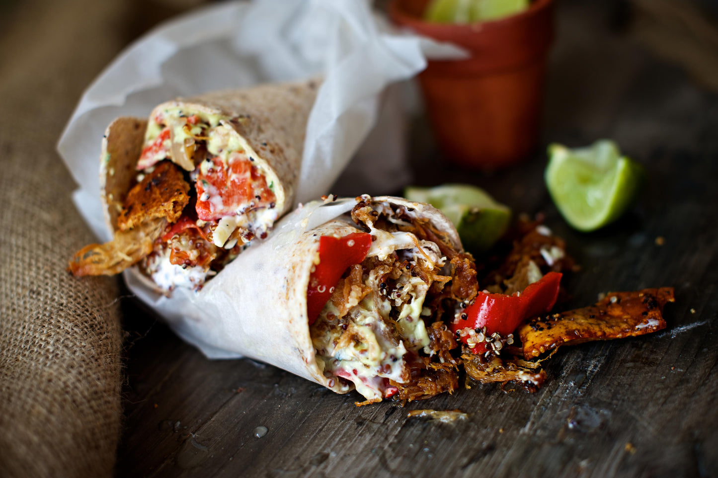 Burritos stuffed with quinoa, pork and refried beans wrapped in paper with wedges of lemon on the side