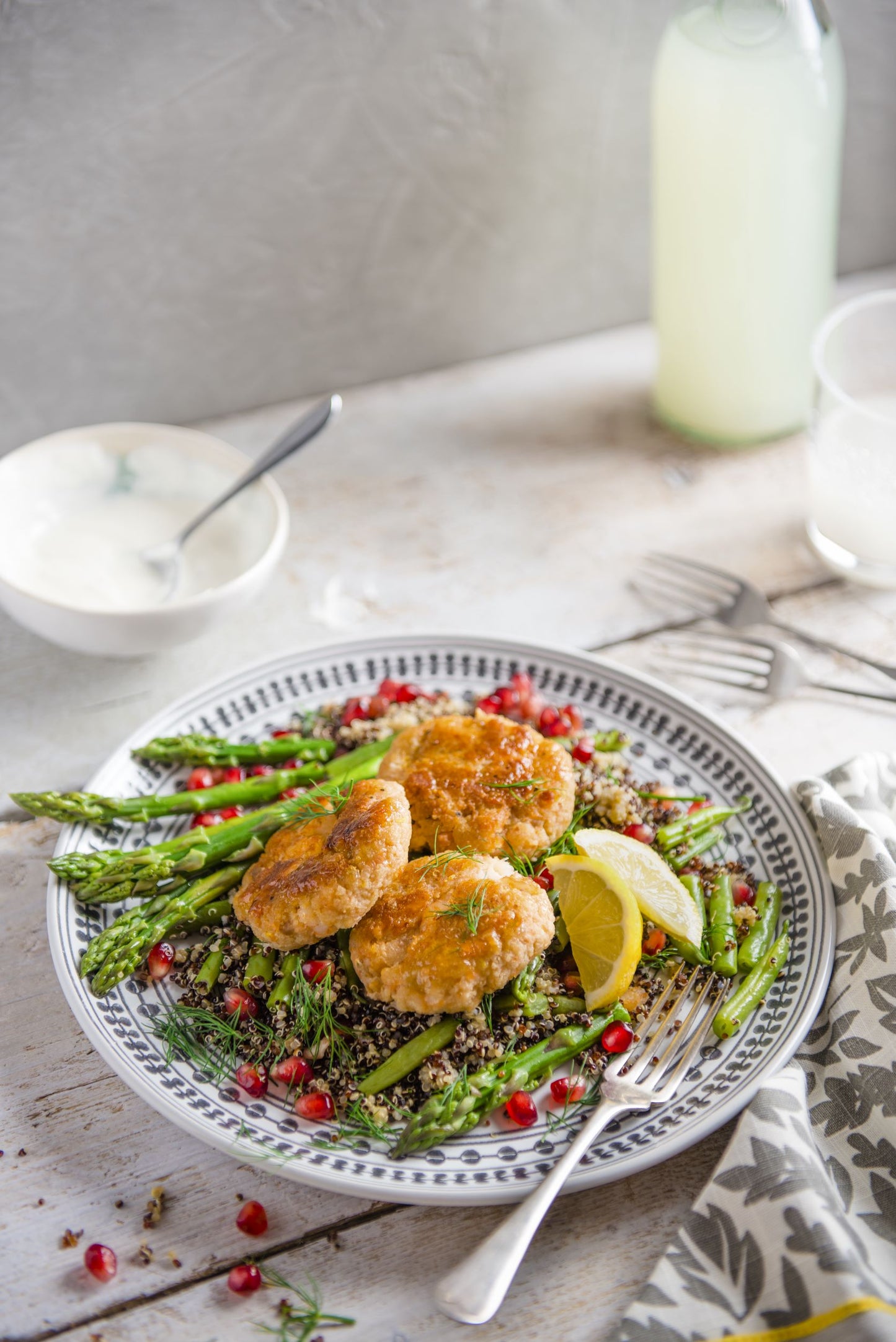 Plate of quinoa and asparagus with salmon fishcakes and wedges of lime  