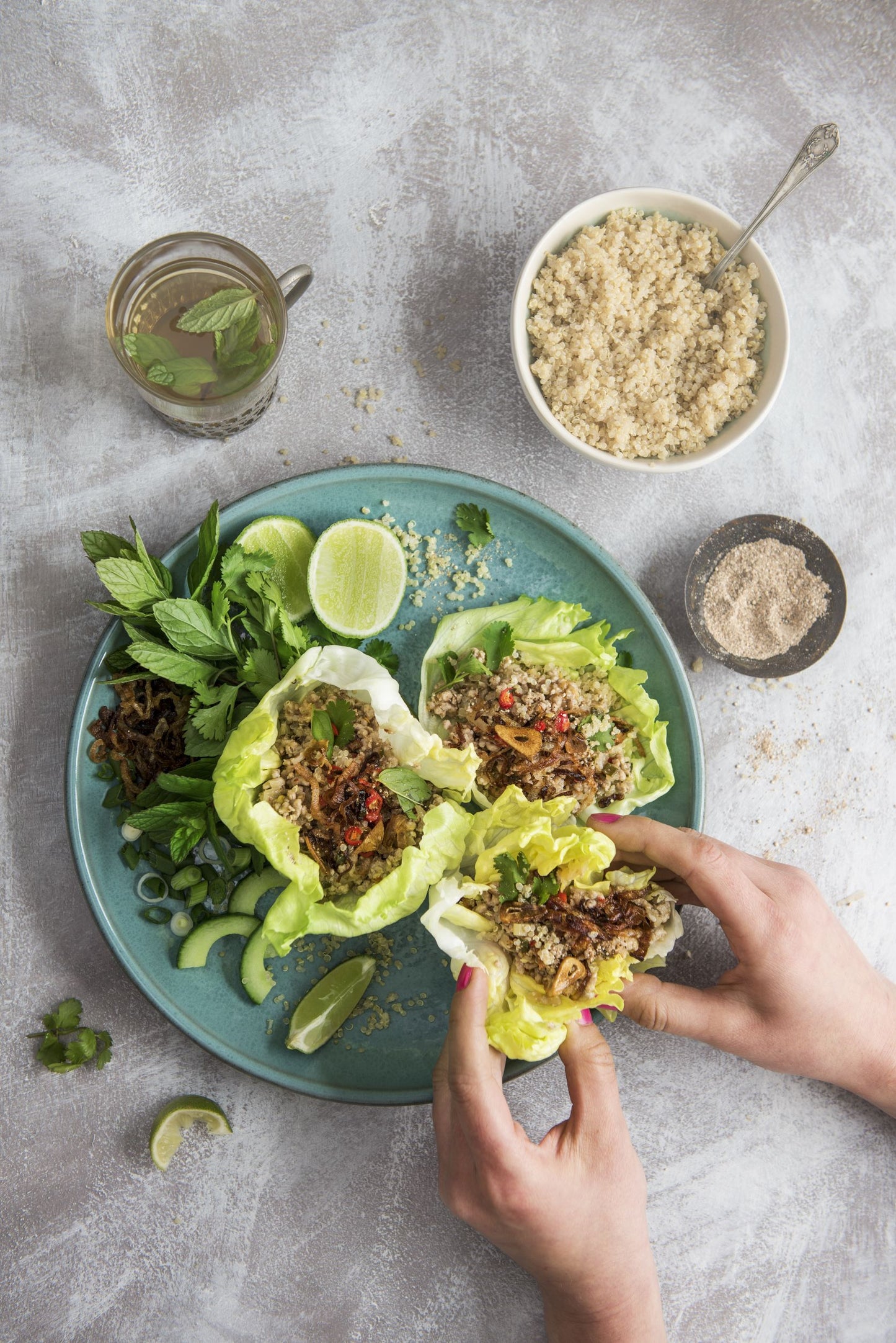 Plate of lettuce leaves filled with quinoa and minced pork. A hand is picking up a lettuce wrap. 