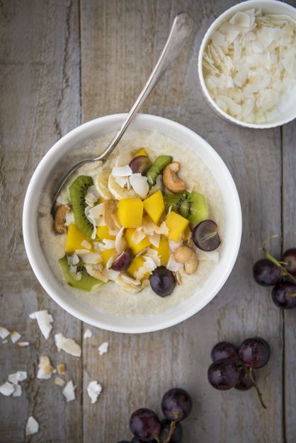 Bowl of porridge made from quinoa flakes, topped with kiwi, mangoes, grapes and coconut flakes