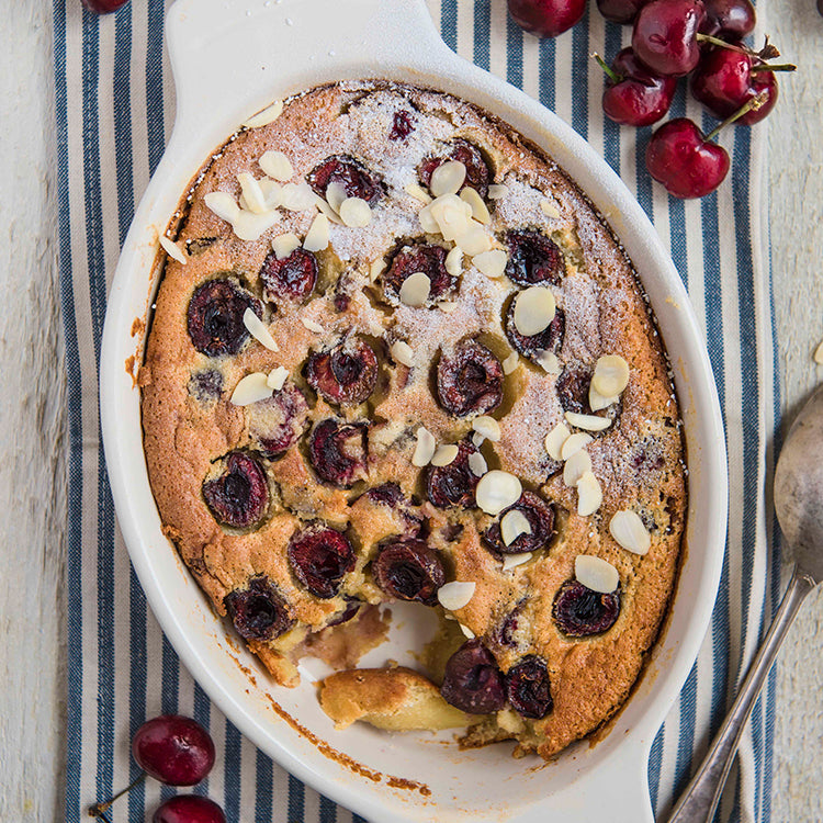Baking tin filled with quinoa cherry cake with cherries dotted around the edge