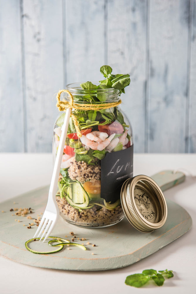 A large jar filled with quinoa, prawns and  herby salad. A fork is placed against the jar